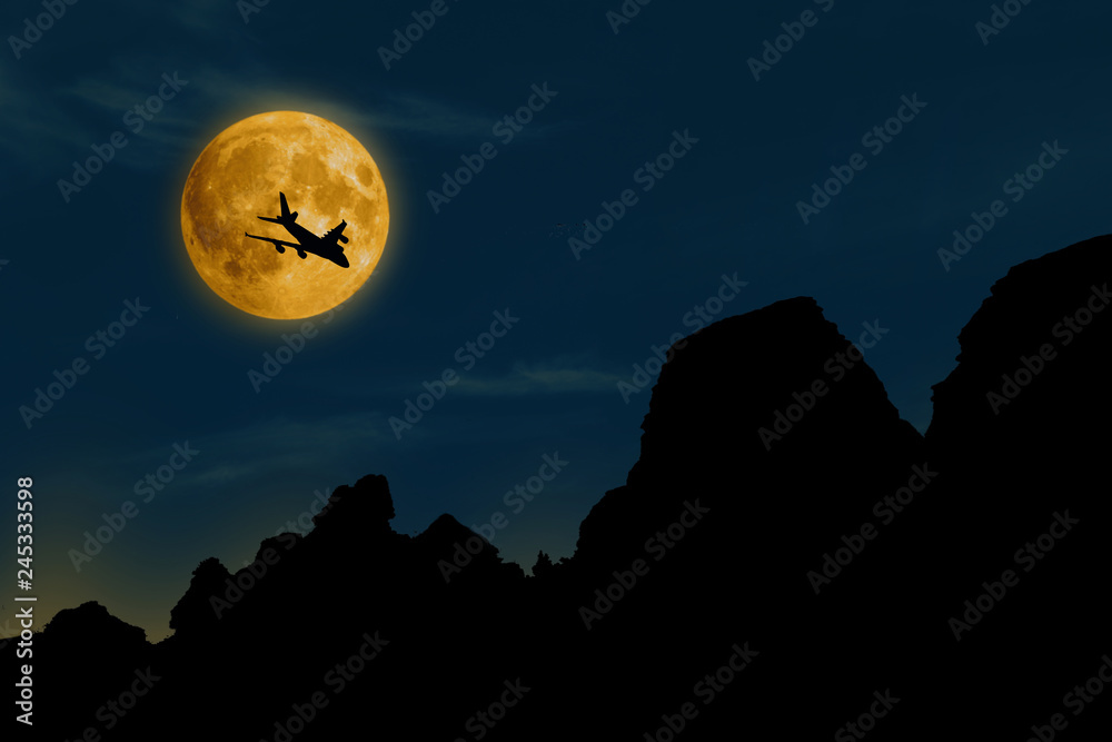silhouette of airplane on moon backgtound in blue sky over mountains