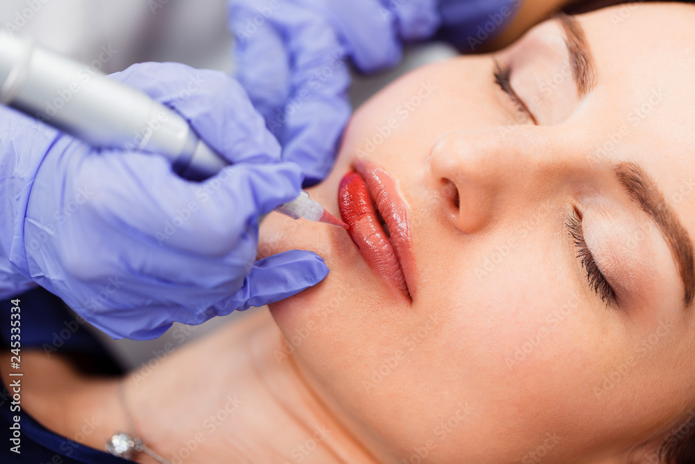 Young woman having permanent makeup on lips in beautician salon. Close up