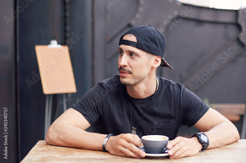Handsome confident guy in hat, sporty stylish clothes, turned back noticing beautiful female student, wants to flirt with lady while drinking coffee at modern cafe with mock up menu list on background