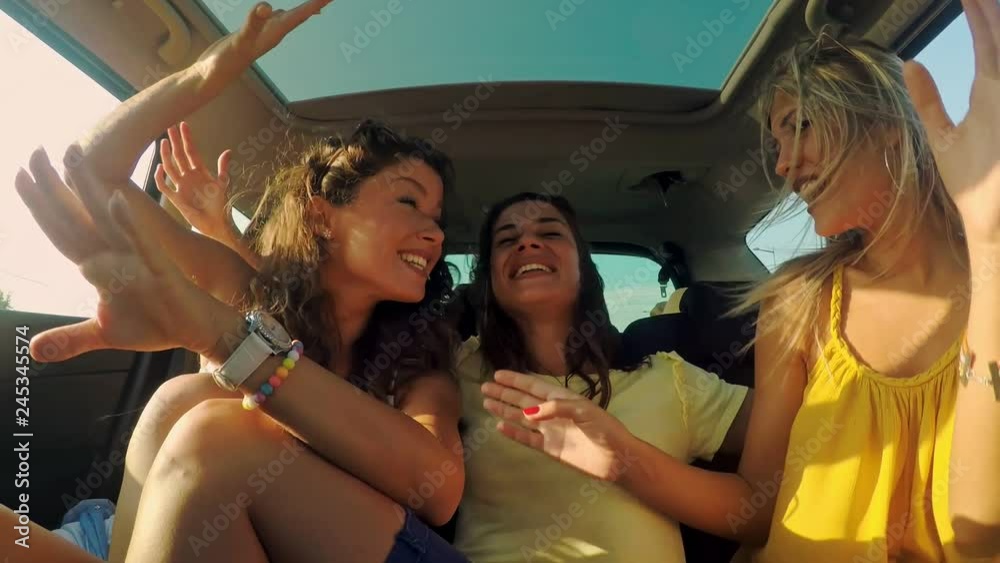 Three female friends enjoying traveling in the car. Sitting in rear seat and having fun on a road trip.