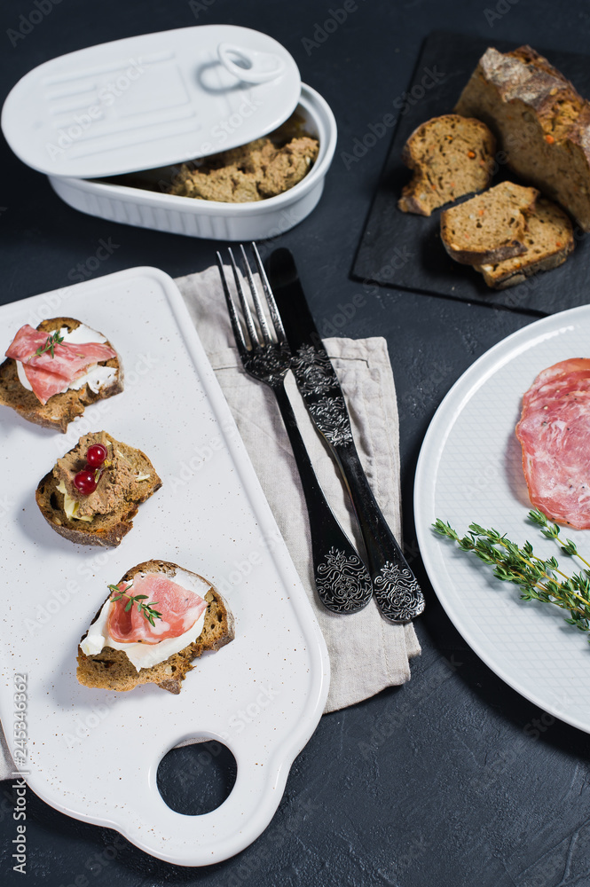 Italian bruschettes with Parma, salami and pate. Plate of pate, salami. Bread on a black stone Board. Black background.