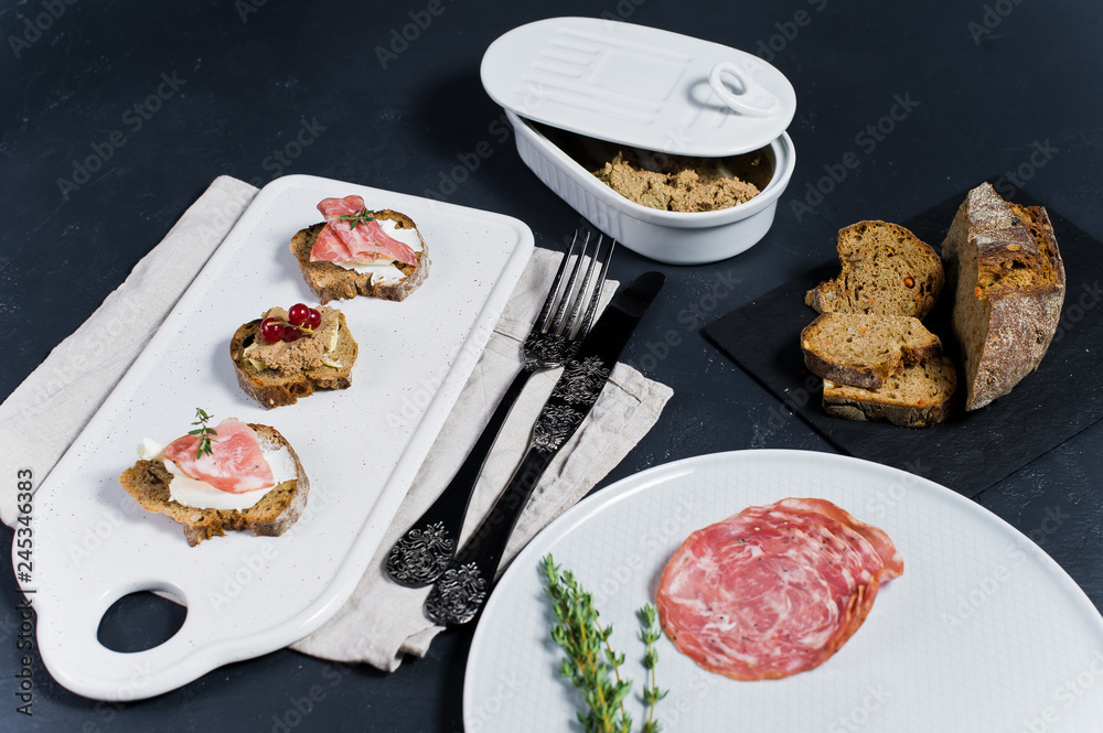 Italian bruschettes with Parma, salami and pate. Plate of pate, salami. Bread on a black stone Board. Black background.