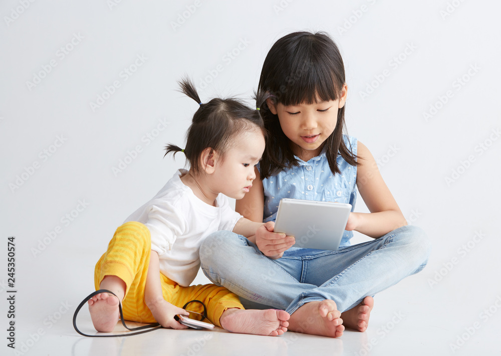Asian little sisters are playing with digital product, on white background Asian little sisters are playing with digital product, on white background