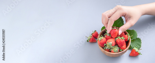 Fototapeta Naklejka Na Ścianę i Meble -  A young woman is holding a bowl of strawberries isolated on a airy blue background, closeup, topview, copyspace.