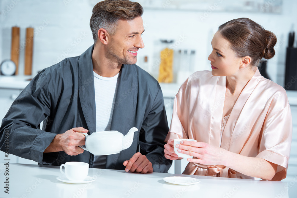 selective focus of beautiful adult couple in robes having tea in kitchen selective focus of beautiful adult couple in robes having tea in kitchen