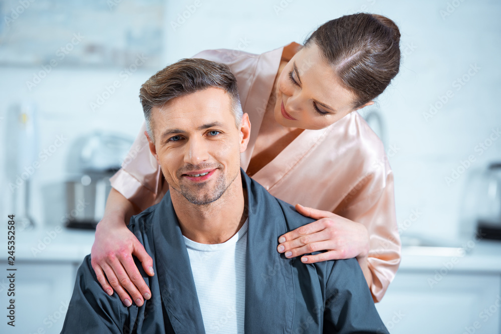 Fototapeta premium beautiful woman in robe embracing smiling man in kitchen