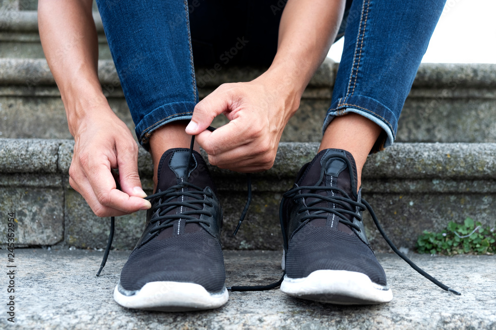 man tying or untying the shoelaces of his sneakers