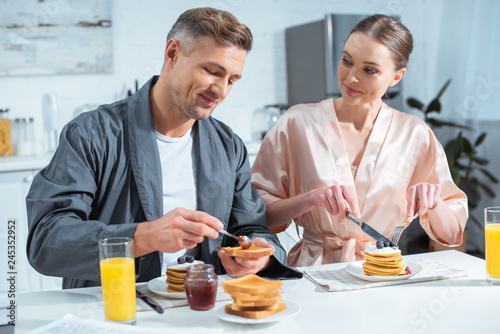 selective focus of husband and wife in robes during breakfast with pancakes and orange juice in kitchen © LIGHTFIELD STUDIOS