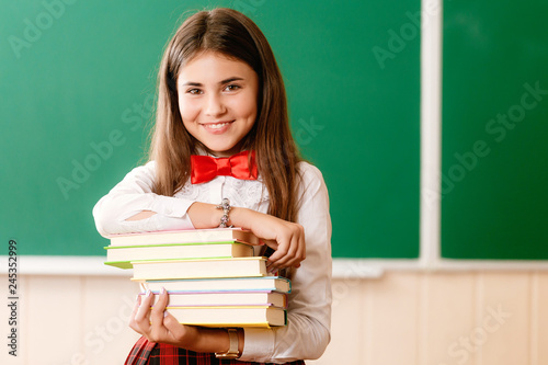 beautiful schoolgirl in red school uniform standing with books in front of the blackboard
