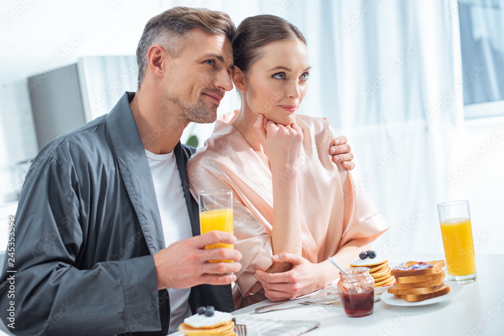 handsome man holding orange juice and hugging woman during breakfast in morning handsome man holding orange juice and hugging woman during breakfast in morning