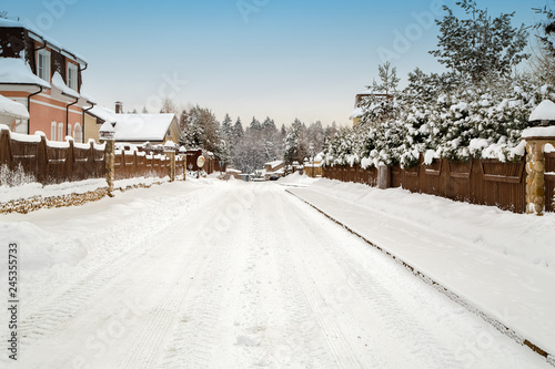 Snowy road between country houses. Christmas winter landscape.Blue sky and forest as background. Country life concept