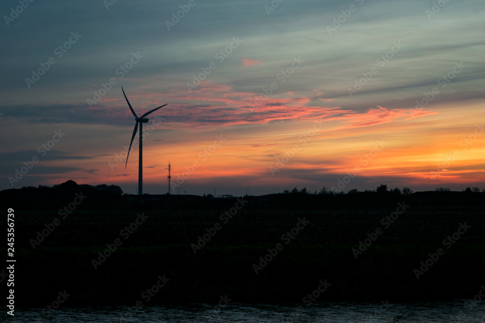 Obraz premium Wind turbine silhouette at colorful sunset over rural landscape