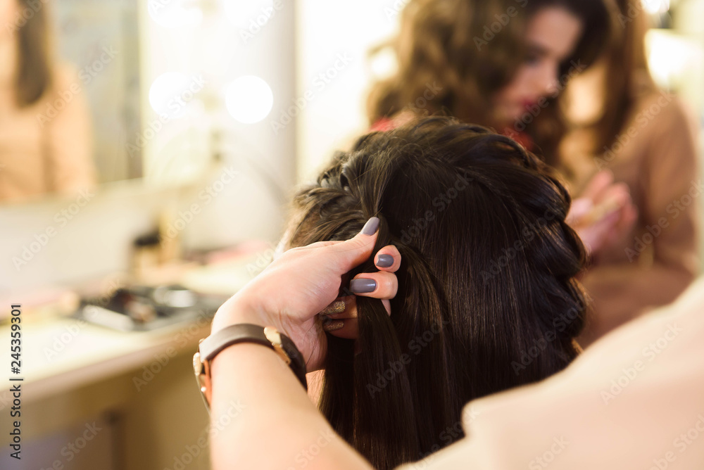 Naklejka premium Beautiful girl with long hair, hairdresser weaves a French braid, in a beauty salon. Professional hair care and creating hairstyles.