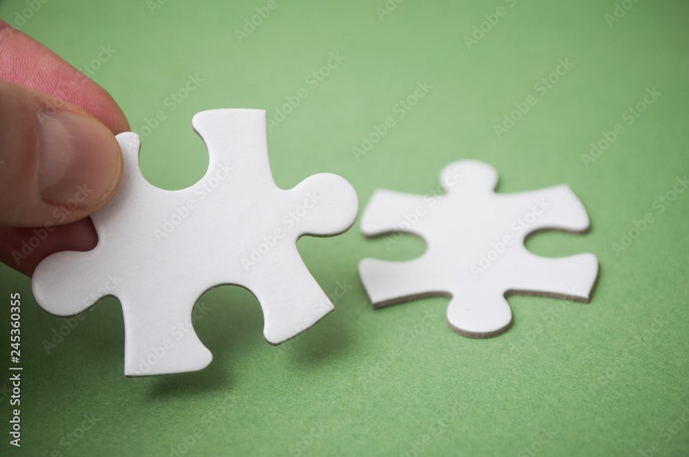 Obraz premium man connecting with hand two jigsaw puzzle pieces on green background. The concept of finding the right solutions in teamwork.