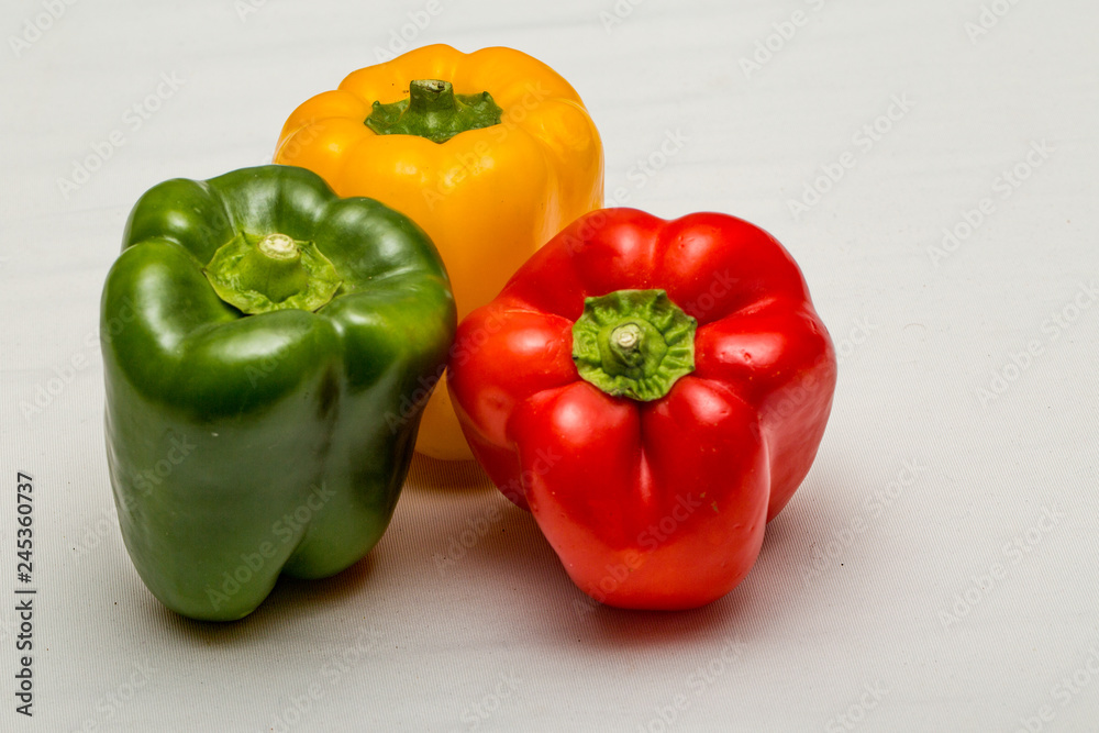 Close up of green pepper, yellow pepper and red pepper isolated against a plain white background Close up of green pepper, yellow pepper and red pepper isolated against a plain white background