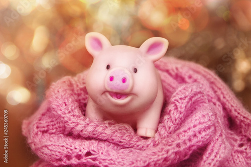 smiling rubber pig toy stands in a woolen openwork scarf against a background of yellow bokeh