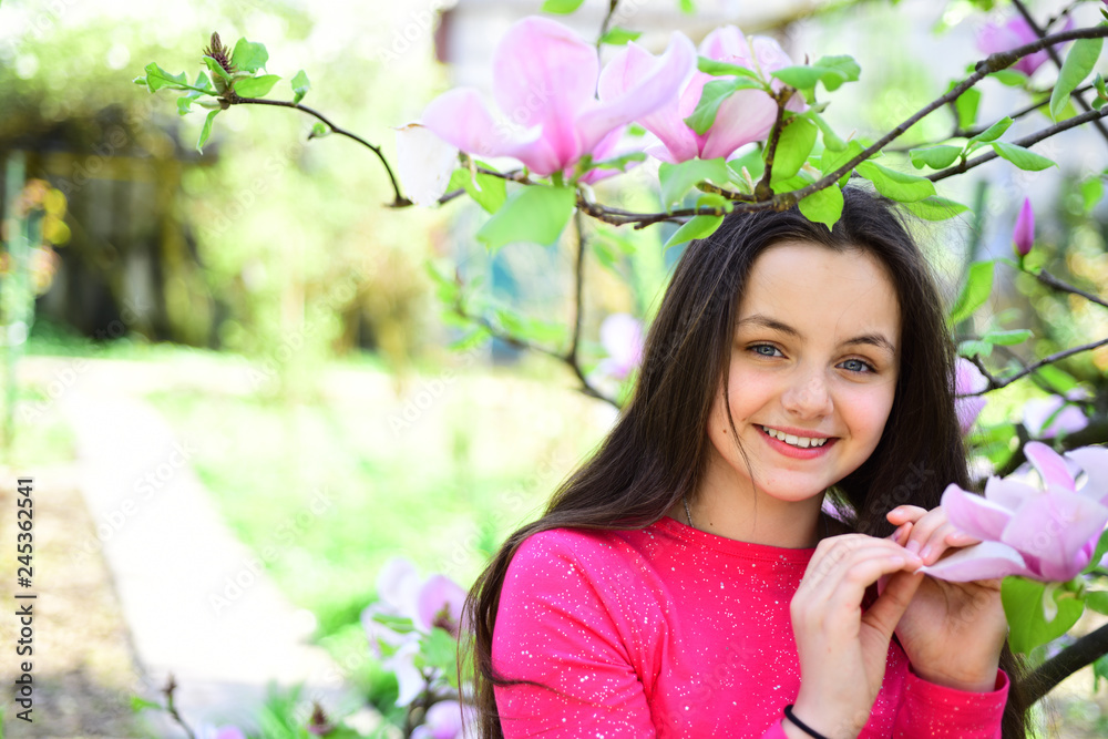 Spring mood. Adorable girl smile in park with blossoming flowers. Its spring time. Pretty girl near flowering tree enjoy magnolia blossom. Cute girl happy smiling on spring landscape Spring mood. Adorable girl smile in park with blossoming flowers. Its spring time. Pretty girl near flowering tree enjoy magnolia blossom. Cute girl happy smiling on spring landscape