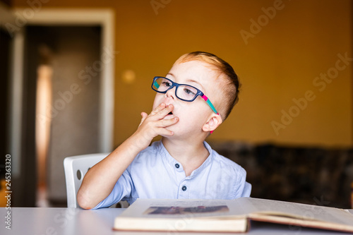 Cute toddler boy with down syndrome with big glasses reading intesting book