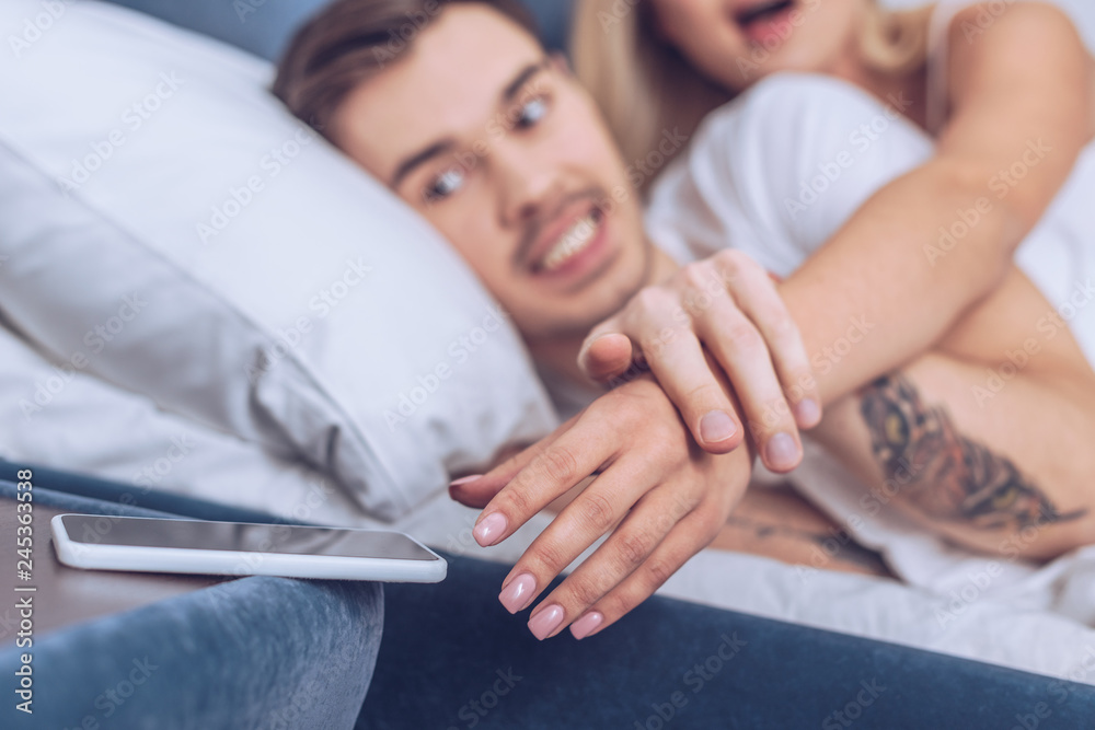 cropped shot of angry man holding hand of wife reaching for smartphone in bedroom cropped shot of angry man holding hand of wife reaching for smartphone in bedroom