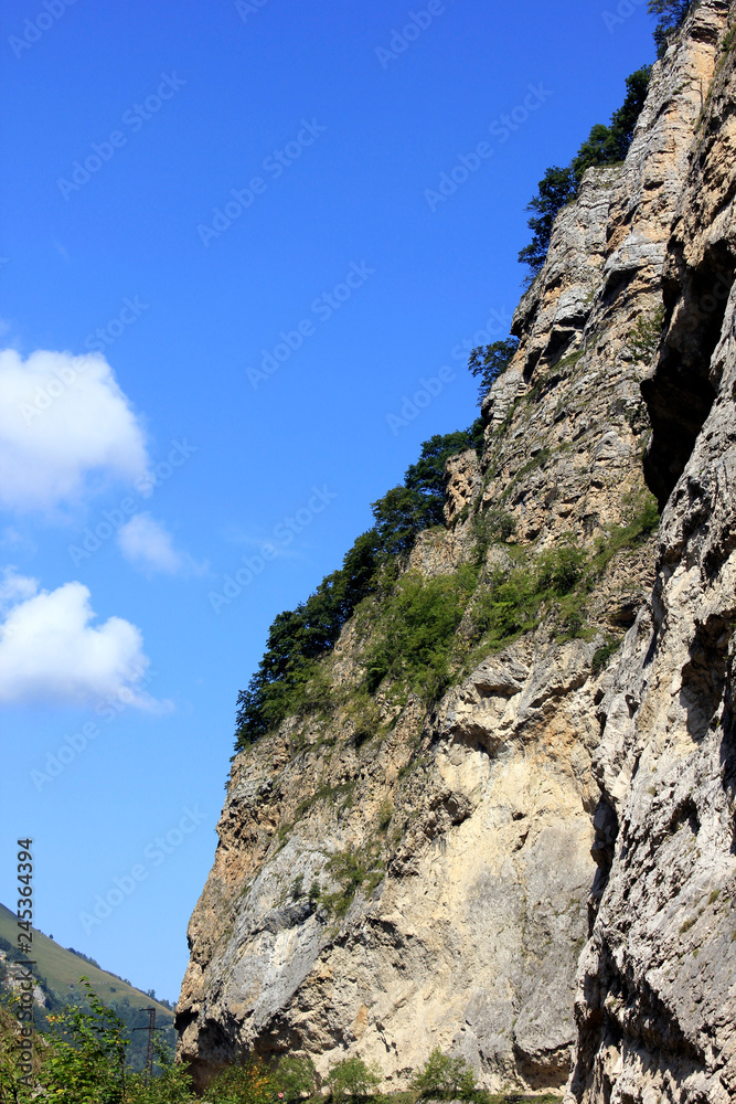 slopes of the Caucasian mountains with green trees against a blue sky with clouds slopes of the Caucasian mountains with green trees against a blue sky with clouds