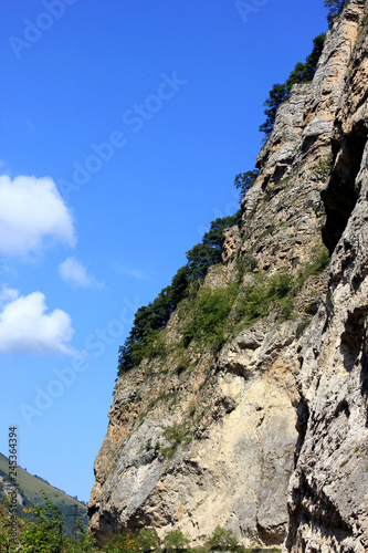 slopes of the Caucasian mountains with green trees against a blue sky with clouds