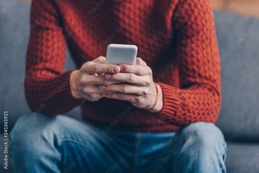 cropped shot of young man in red sweater using smartphone at home cropped shot of young man in red sweater using smartphone at home