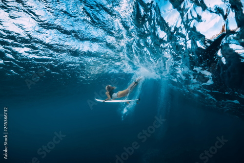 Surf woman with surfboard dive underwater with under wave.