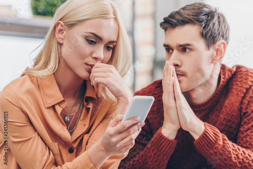 young man looking at girlfriend using smartphone at home, distrust concept