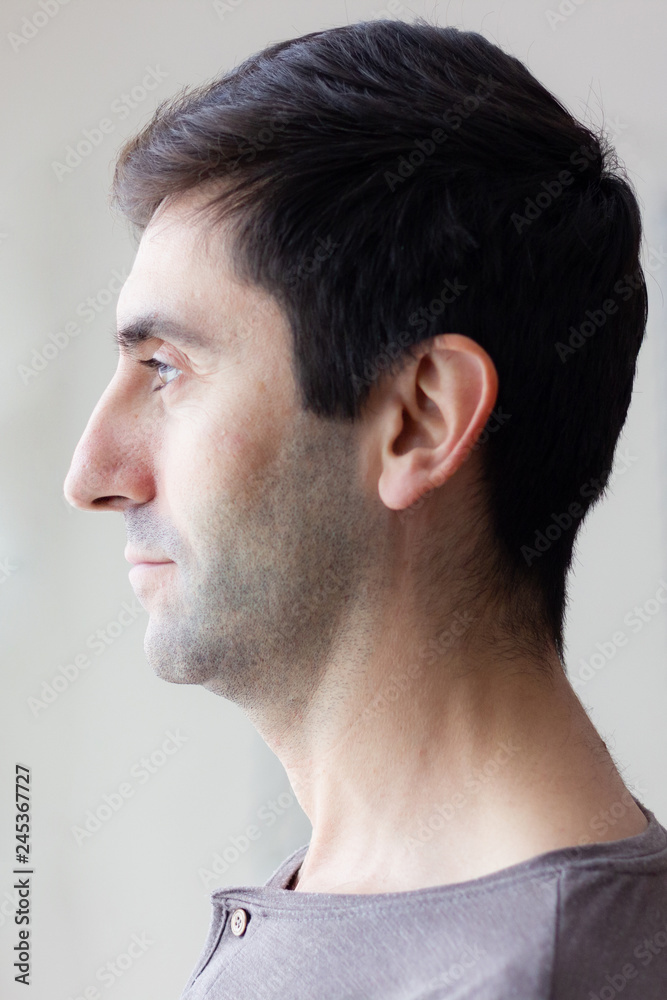 Obraz premium Profile of handsome man on studio. Young model portrait looking to the side over white background. Fashion, style, natural light, photoshoot concepts