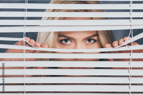 young woman looking at camera and peeking through blinds