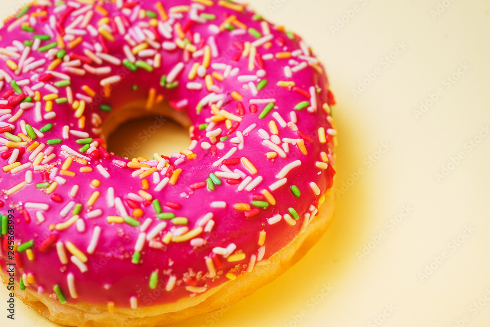 Bright donut in a pink glaze with a multi-colored rainbow sprinkle on a yellow background. Bright donut in a pink glaze with a multi-colored rainbow sprinkle on a yellow background.