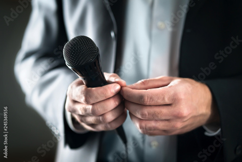 Stage fright concept. Nervous and shy public speaker with microphone. Business man afraid of giving speech for crowd of people or audience. Sweaty hands holding mic. Bad presentation. Stressed singer.