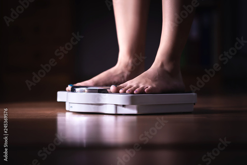 Feet on scale. Weight loss and diet concept. Woman weighing herself. Fitness lady dieting. Weightloss and dietetics. Dark late night mood.