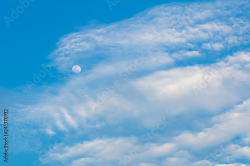 Bright blue morning sky with the half moon and clouds. The moon and clouds in the summer sky . moon in the morning time with blue sky background, clear morning sky with bright growing moon 