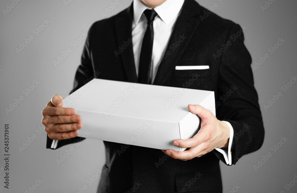 Businessman in a black suit holding a white box. Close up. Isolated background Businessman in a black suit holding a white box. Close up. Isolated background