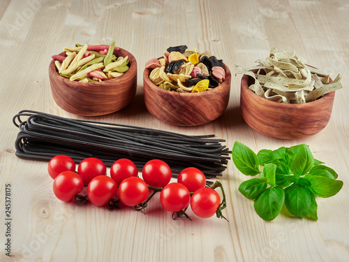 Dried pasta: colorful orechiette, fusilli , tagliatelle, spaghetti, fresh tomatoes and basil, on a wooden board