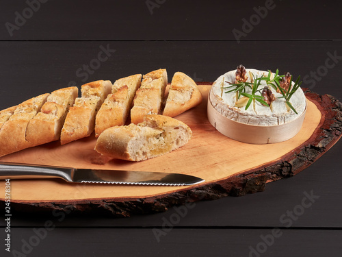 Baked Camembert with walnuts, rosemary stalks and garlic cloves, served with crusty garlic gread, on a rustic board photo