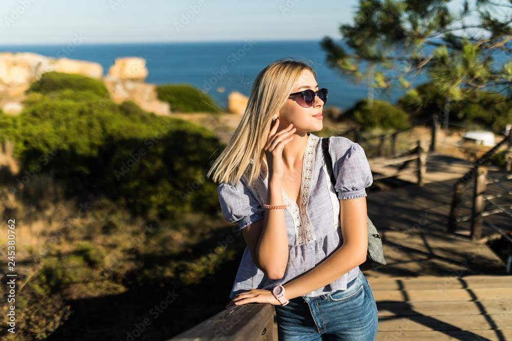 Young blonde woman in sunglasses with bag walking on the stair on the way to the sea beach