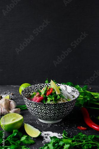 Pho Bo vietnamese soup with noodles, beef, chili pepper, onion,  cilantro and lime on dark black background with copy space on top