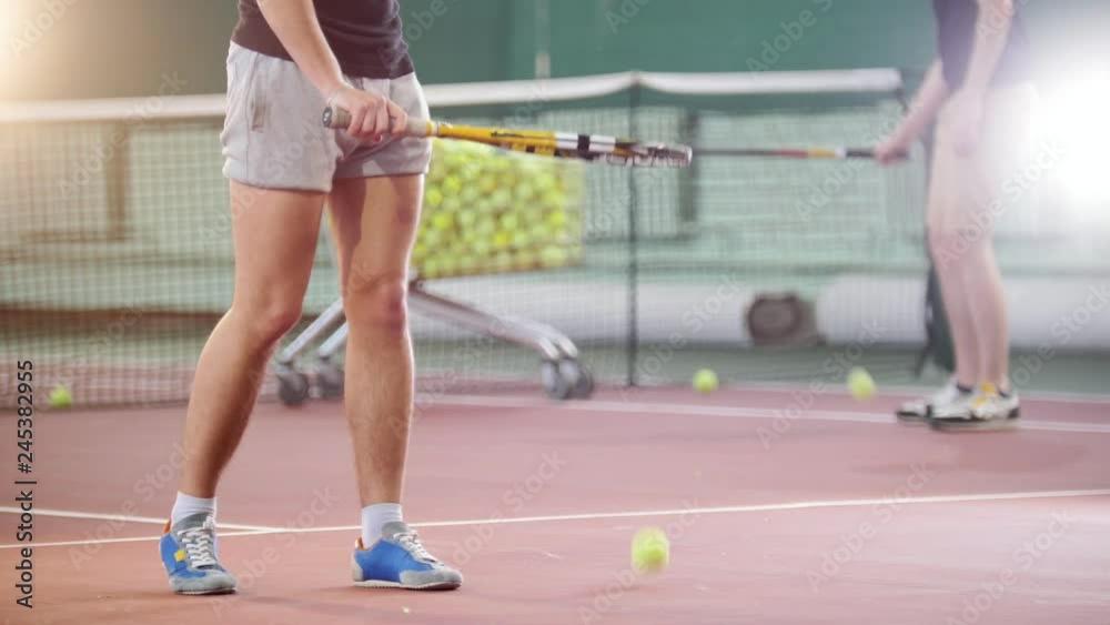 Training on the tennis court. Two young men hitting the ball from the floor. Legs in focus Training on the tennis court. Two young men hitting the ball from the floor. Legs in focus