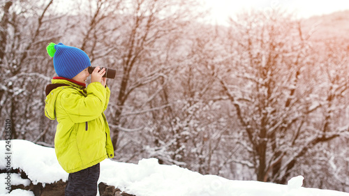 Little explorer with monocular at winter nature. Сute kid nature explorer in winter forest. Winter vacation. Happy childhood.