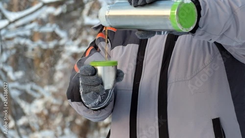 Man in the cold pours hot tea from a thermos into a mug. Hand with a mug of hot tea close-up