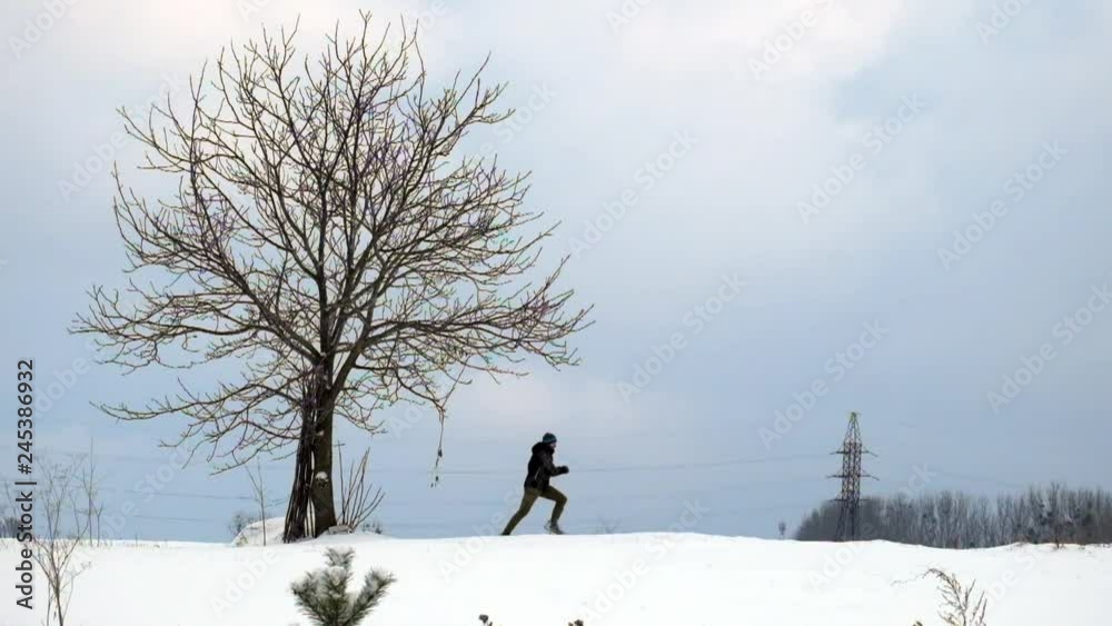 Man runs across a snow-covered field past a lonely bare tree in slow motion Man runs across a snow-covered field past a lonely bare tree in slow motion