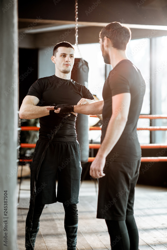 Boxing trainer winding bandage on the wrist for a man, preparing for the boxing on the boxing ring at the gym