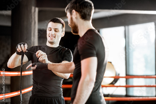 Boxing trainer winding bandage on the wrist for a man, preparing for the boxing on the boxing ring at the gym