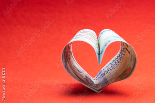 US 100 dollar bill in the shape of a heart on a red background. Concept of money, love and a gift for Valentine's Day. Copy space.