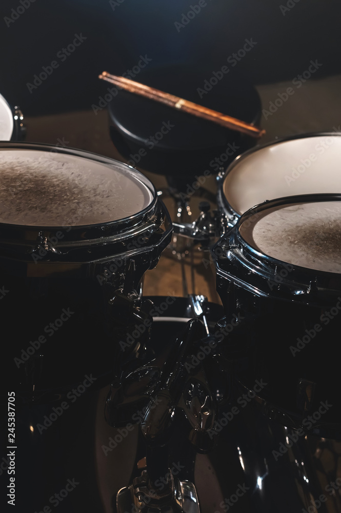 Closeup view of a drum set and Drumsticks in a dark studio. Black drum barrels with chrome trim. The concept of live performances