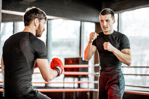 Boxing trainer showing to a man how to fight, teaching to box in the boxing ring at the gym