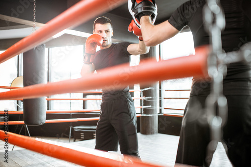 Athletic man fighting during the training with boxing trainer on the boxing ring at the gym