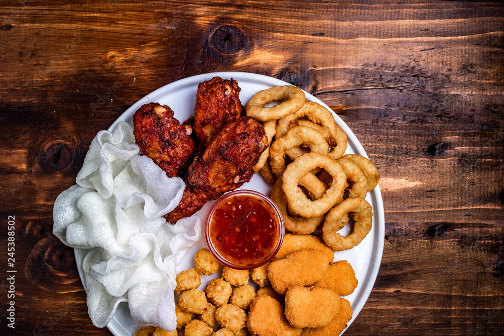 deep-fried beer snacks: chicken nuggets, balls and legs, rice flakes and breaded onion rings. wooden background under the text deep-fried beer snacks: chicken nuggets, balls and legs, rice flakes and breaded onion rings. wooden background under the text